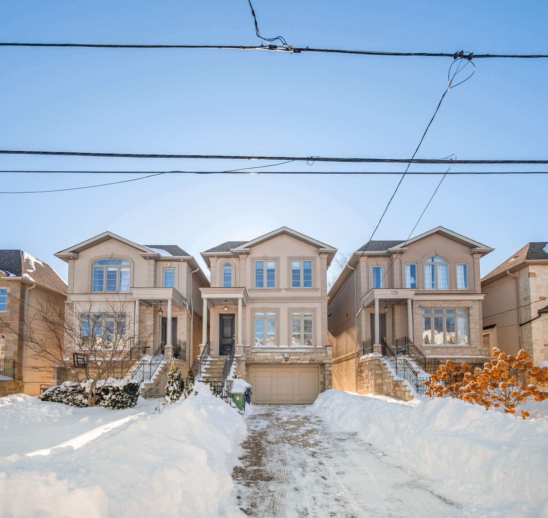 Beige two-story house with a central garage and snow-covered driveway in winter.