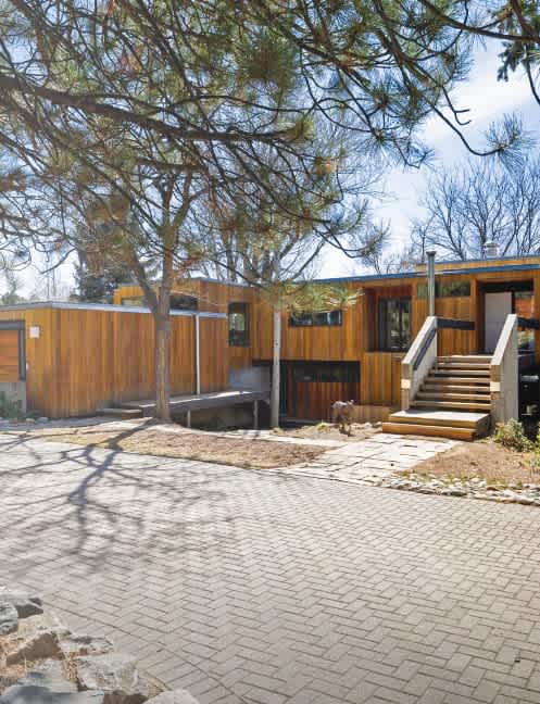 A house with a wooden exterior, brick driveway and stairs leading up to a covered porch