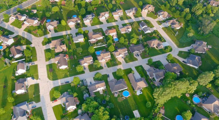 Aerial view showcasing a suburban neighborhood with neatly arranged houses, green lawns, and tree-lined streets.