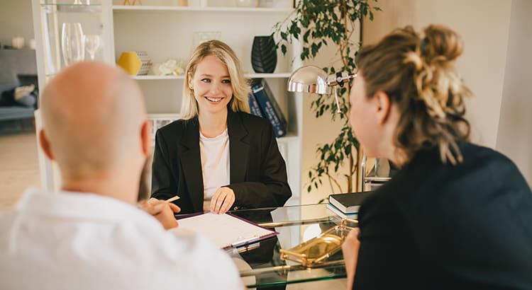 A photo of a professional meeting, with a woman smiling and engaging in a discussion with a client, indicating a real estate or business consultation.