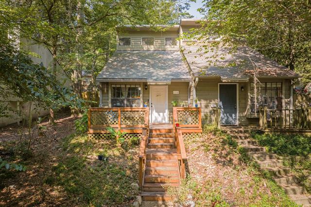 A quaint and rustic house in 114 Meeting St with a stone exterior and a sloping roof. The house is surrounded by trees, giving it a secluded and charming appearance. There is a small staircase leading up to the front entrance.