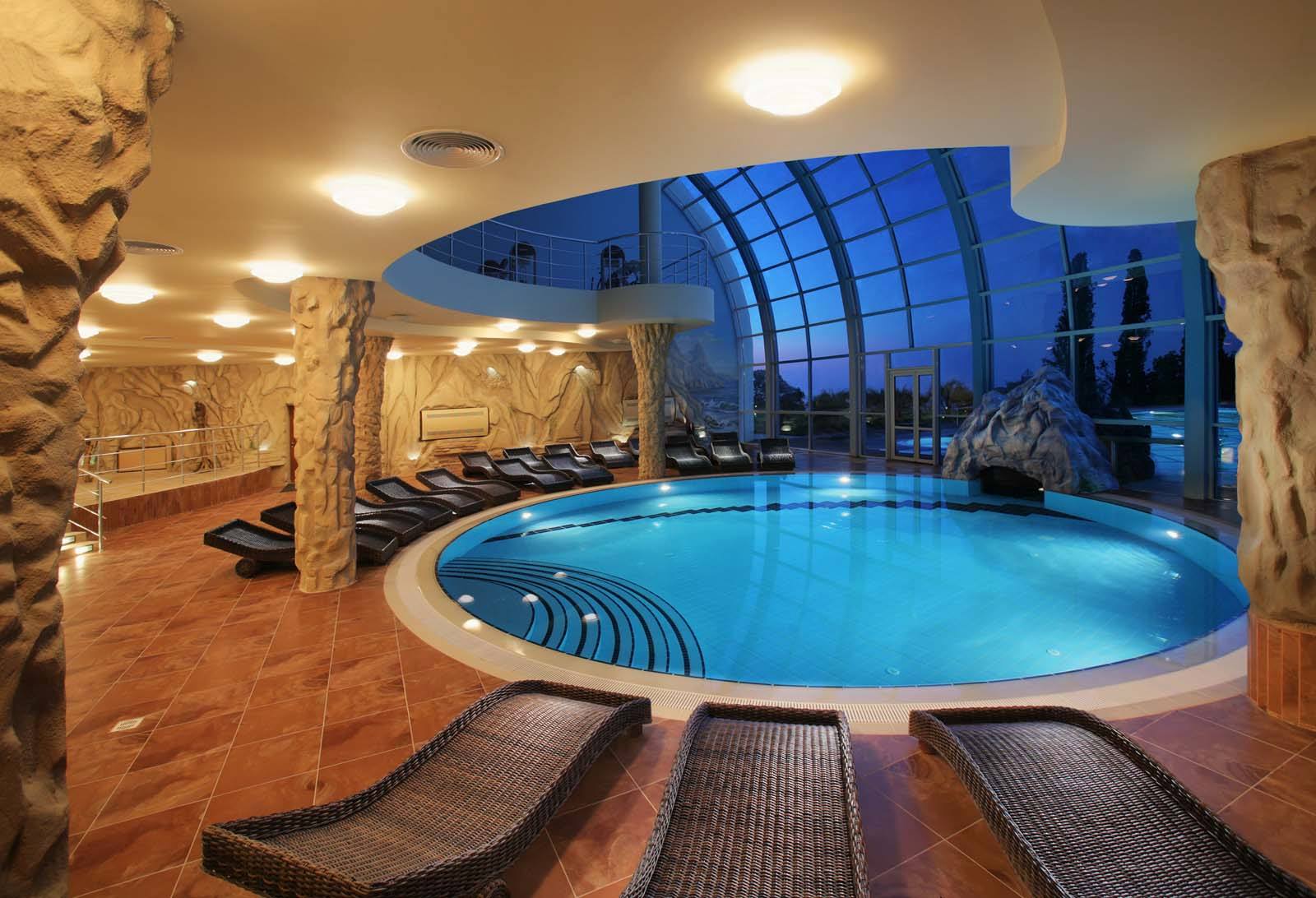 A serene indoor pool area with a curved design, surrounded by lounge chairs and illuminated by soft lighting.