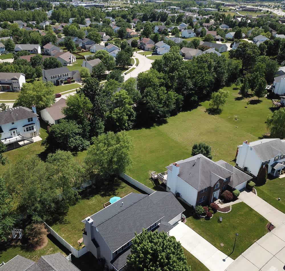 Aerial view of a leafy suburban neighborhood with detached homes and a large grassy open space.