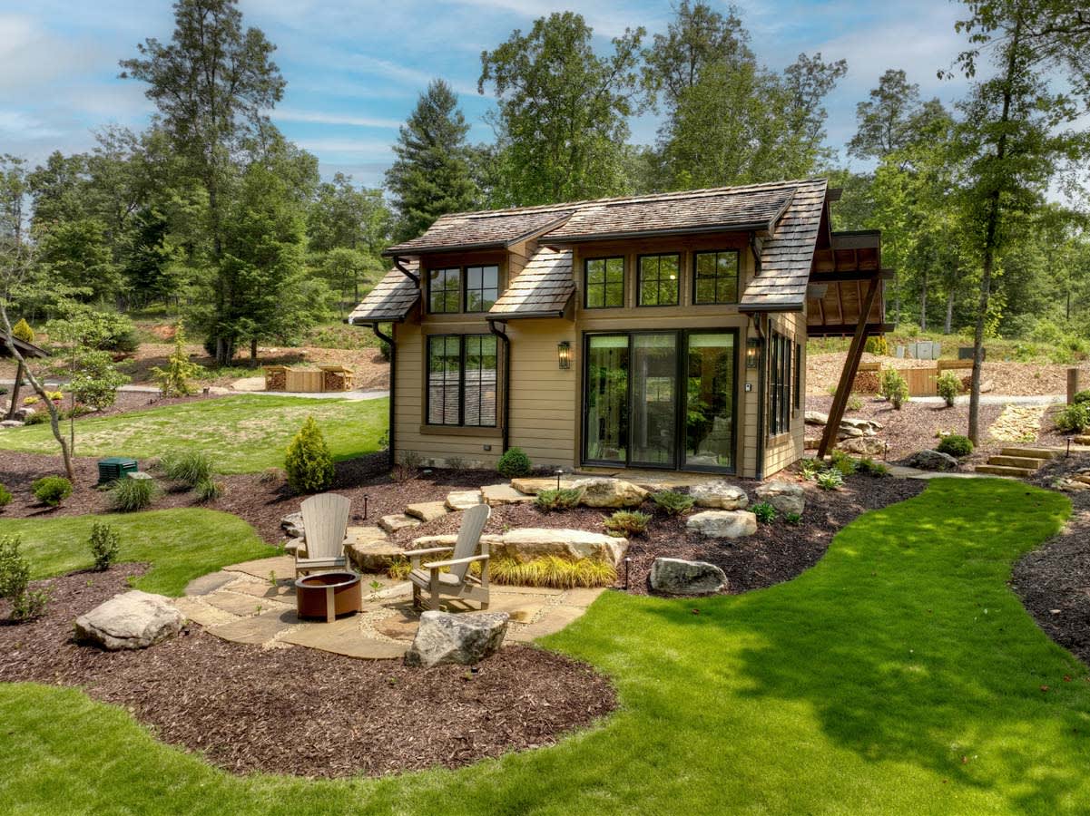 A cozy small house with a glass sliding door and a fire pit in the grassy backyard.