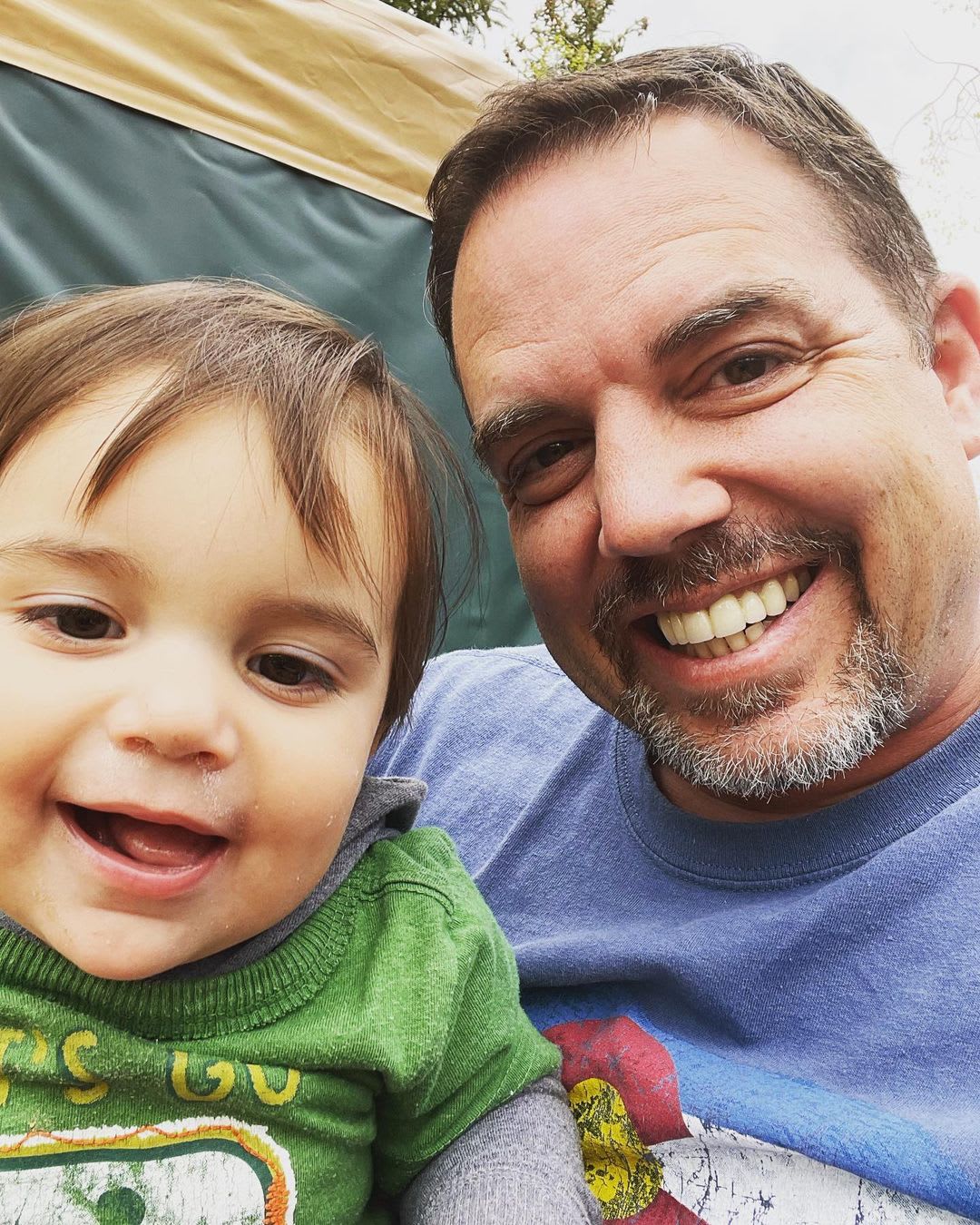 Travis Davis smiling beside a young child in a green shirt.