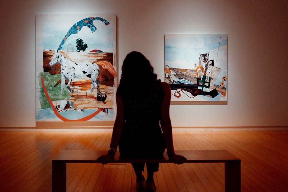 woman sitting, facing art on a wall in a Columbus, Indiana art gallery