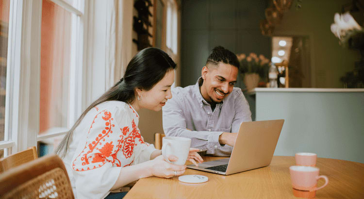 A man and woman are seated at a table, engaged with a laptop, collaborating on a project or discussion.