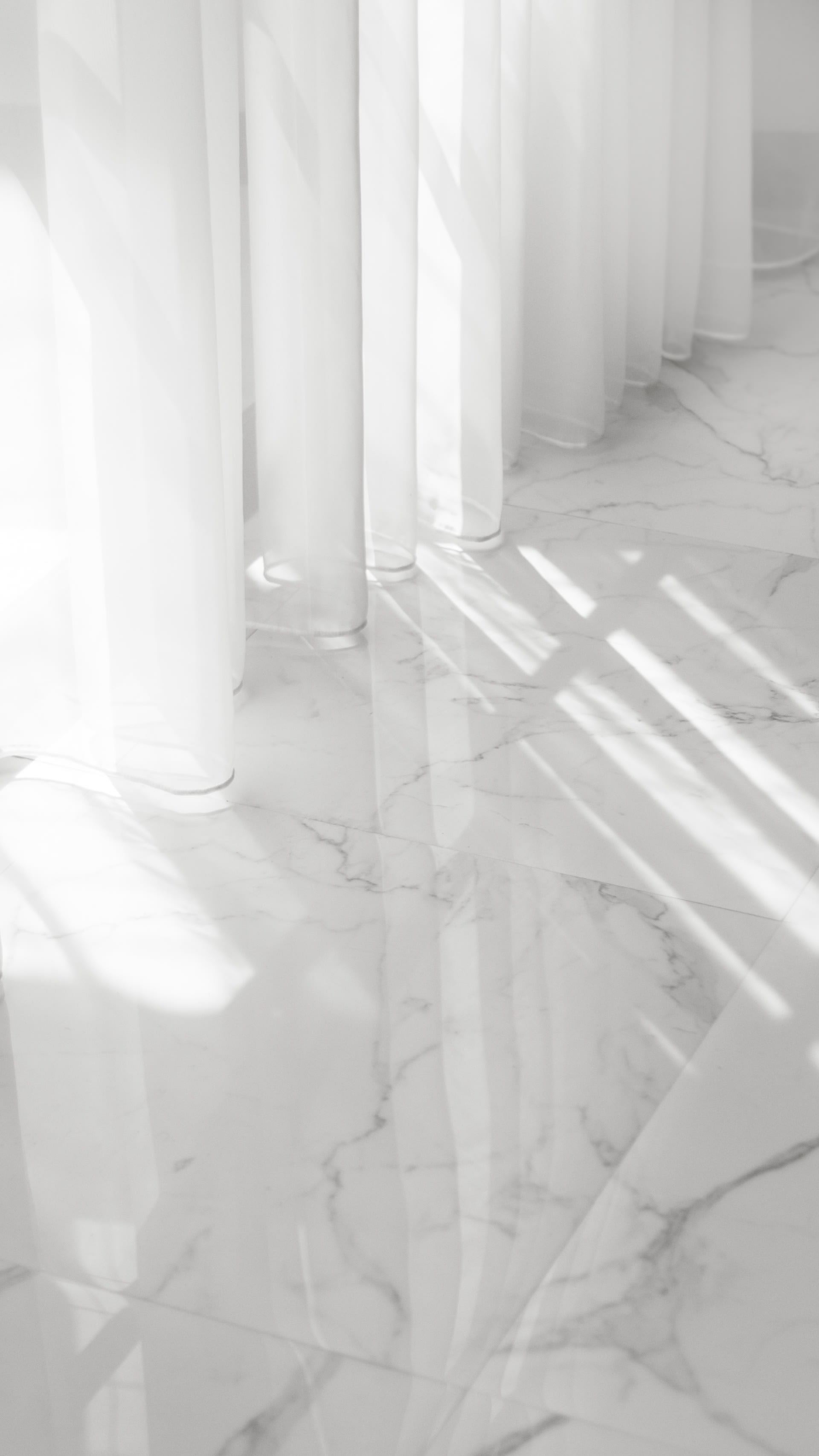 Sheer white curtains cast sunlight across a veined marble floor.