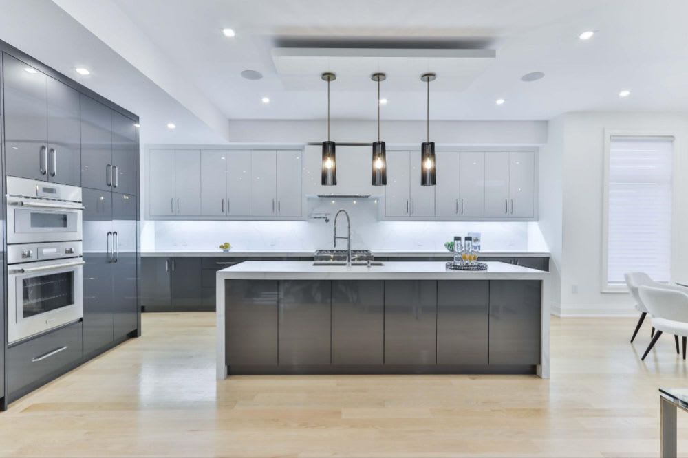 Sleek modern kitchen with gray cabinets, large island, stainless steel appliances, and light hardwood flooring.