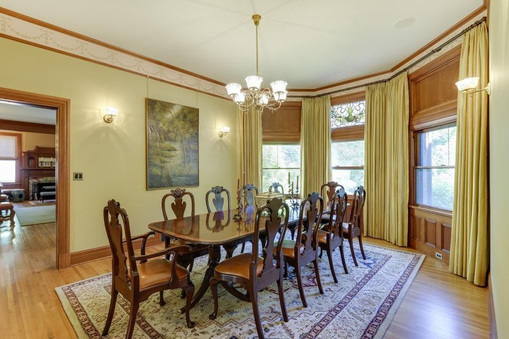 A formal dining room with a round wooden table and cushioned chairs.