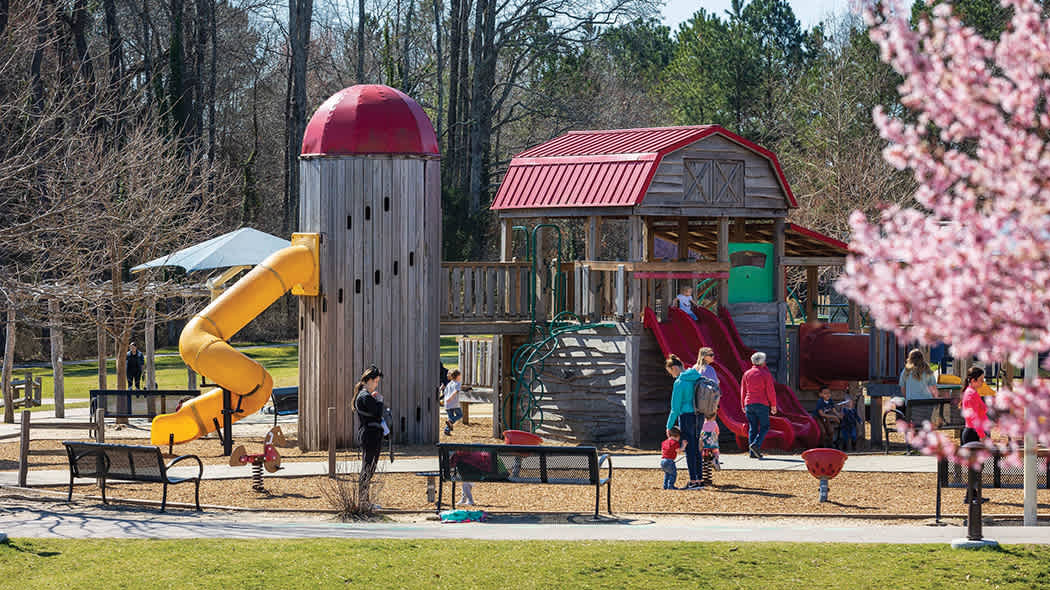 A colorful playground with a slide, climbing structures, and children playing, surrounded by benches and trees.