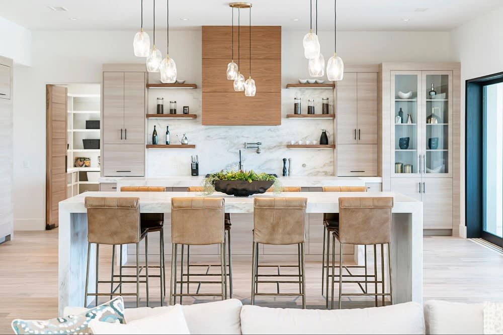 A kitchen with a large island and four bar stools with a white countertop and dark brown cabinets.