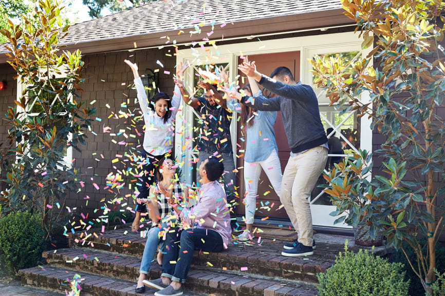 House exterior with a group celebrating on the porch amid colorful confetti.
