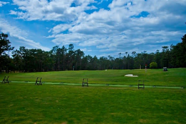 Golf course fairway with a flag, sand bunker, and tree-lined horizon beneath a cloud-filled sky.