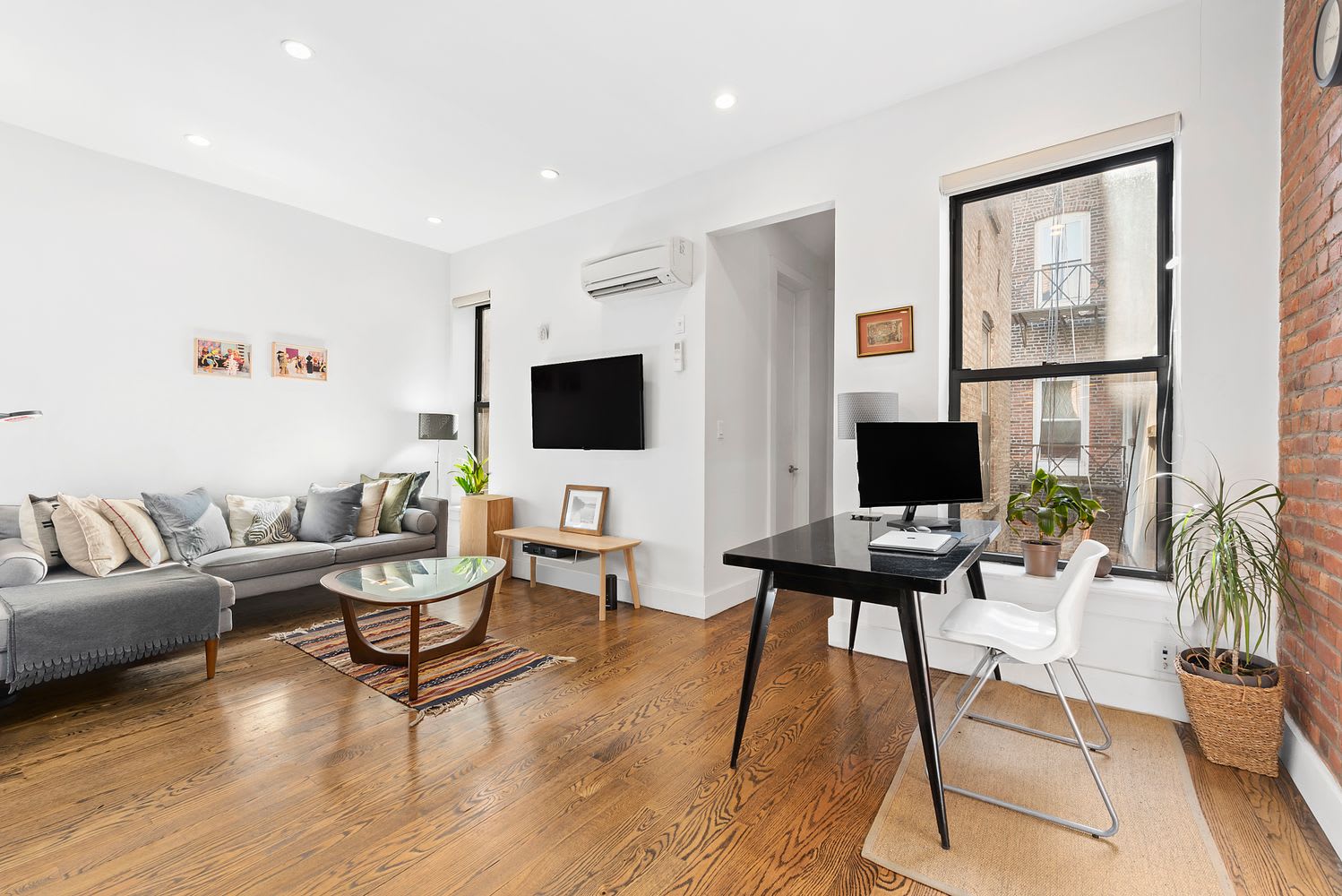 Condo living room with hardwood floors, a gray sectional, large windows, and an exposed brick wall.