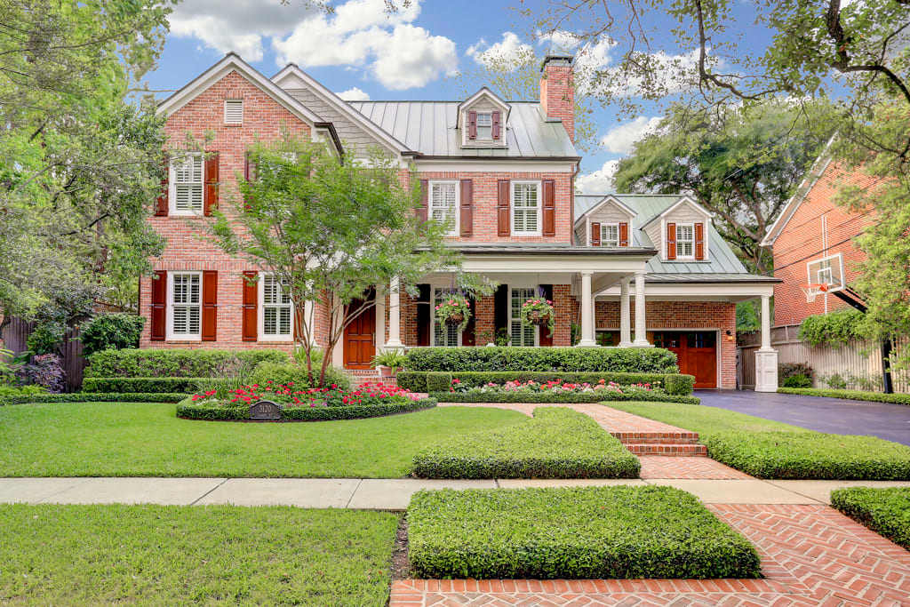 A large, two-story red brick house with a front yard, a paved walkway, and a driveway to a two-car garage on the right.