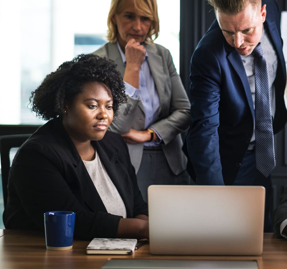 Three colleagues gather around a laptop at an office desk.