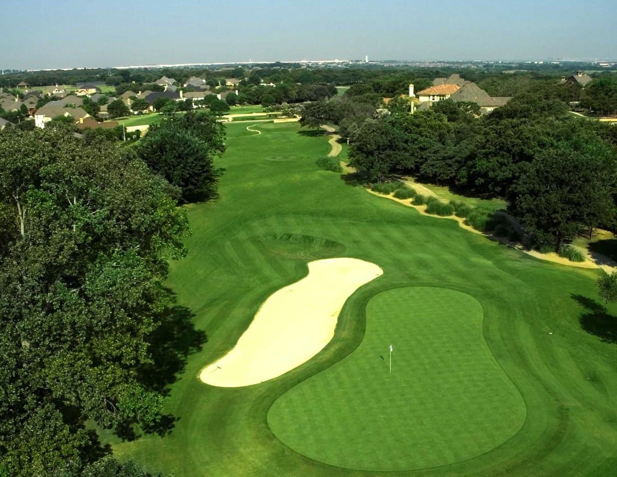 An aerial view of a lush, green golf course on a sunny day. The atmosphere is peaceful, serene, and inviting.