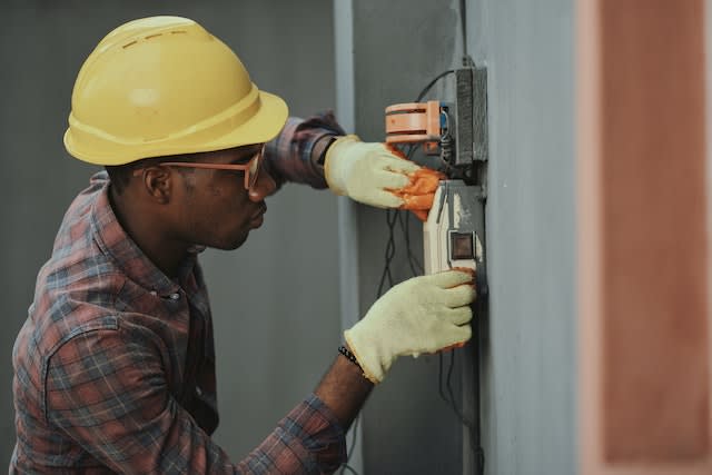 A man with a yellow helmet doing maintenance work around the house