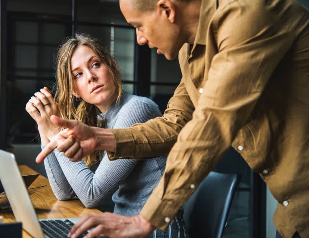 Two people discuss information at a laptop, with one pointing toward the screen.