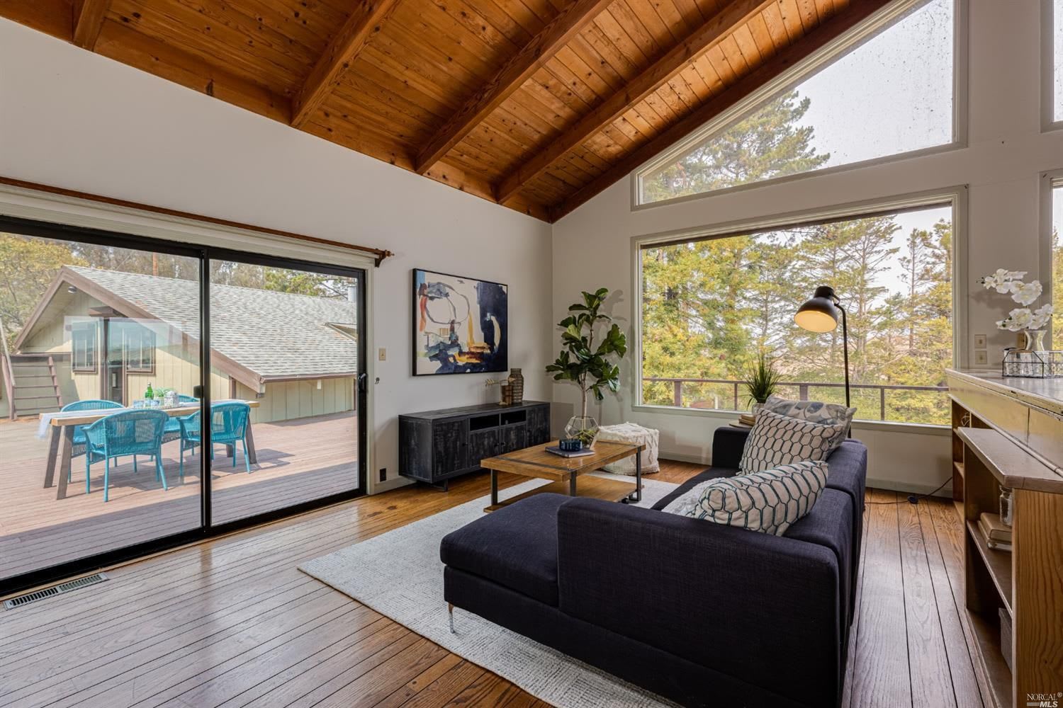 Living room with a vaulted wood ceiling, large windows, and sliding doors to a deck.