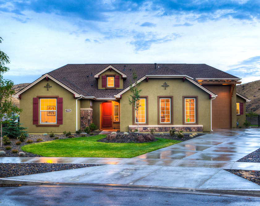 Olive-green single-story home with burgundy trim, stone accents, and a broad wet driveway.