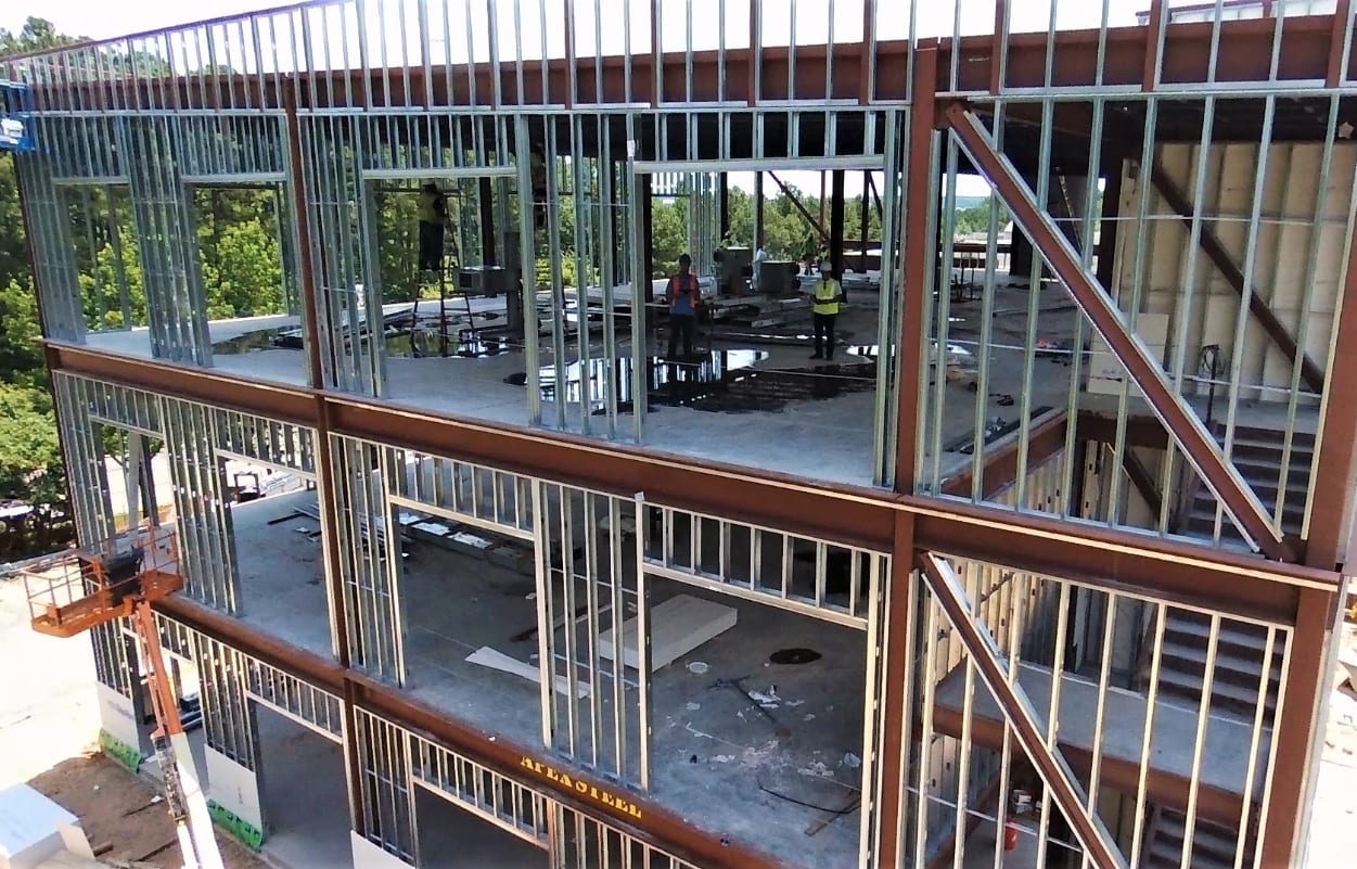 A partially constructed building with metal framing, showing workers inside and a lift outside.