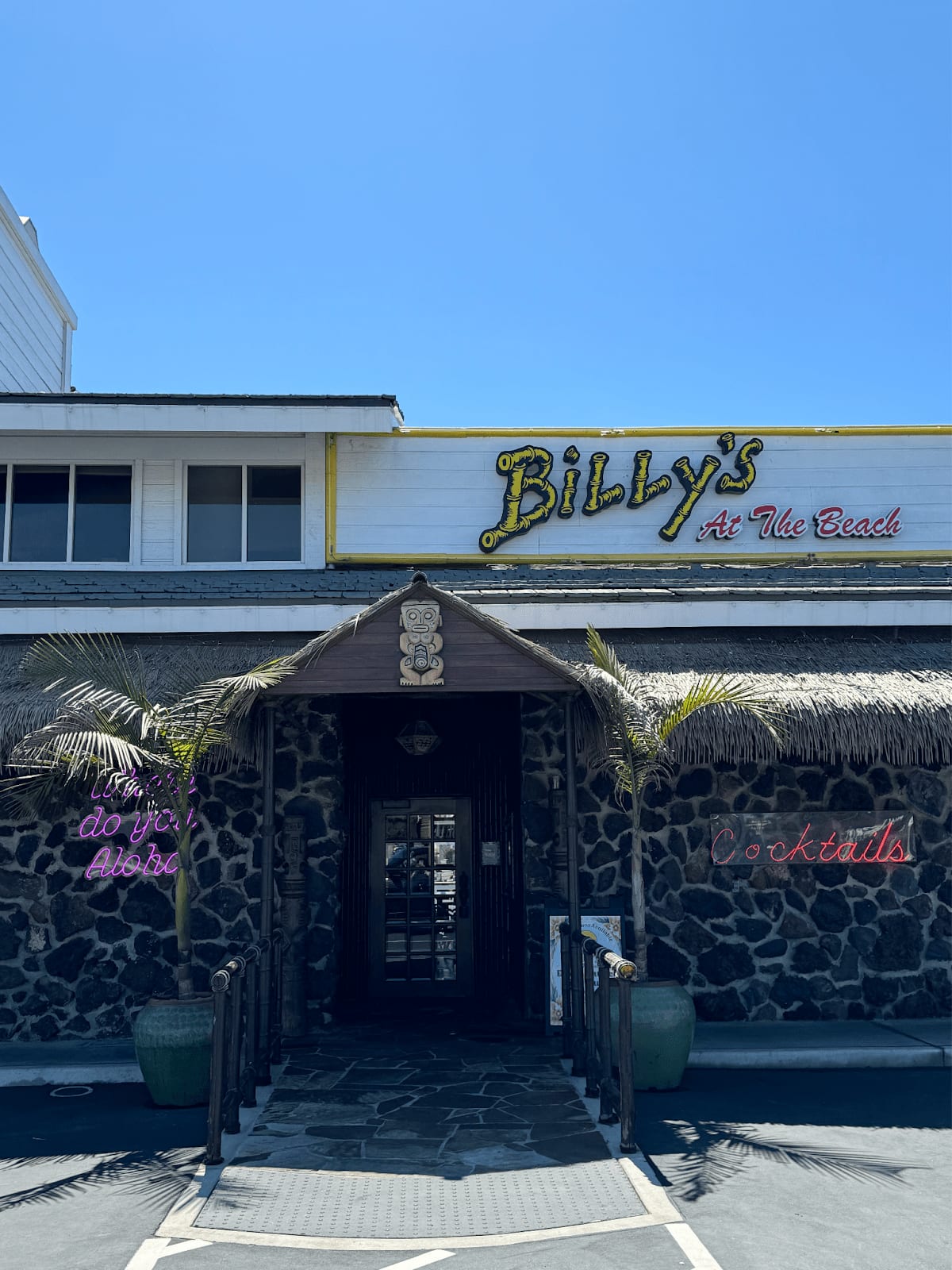 Entrance to Billy's At The Beach restaurant with tiki-themed decor and neon signs.