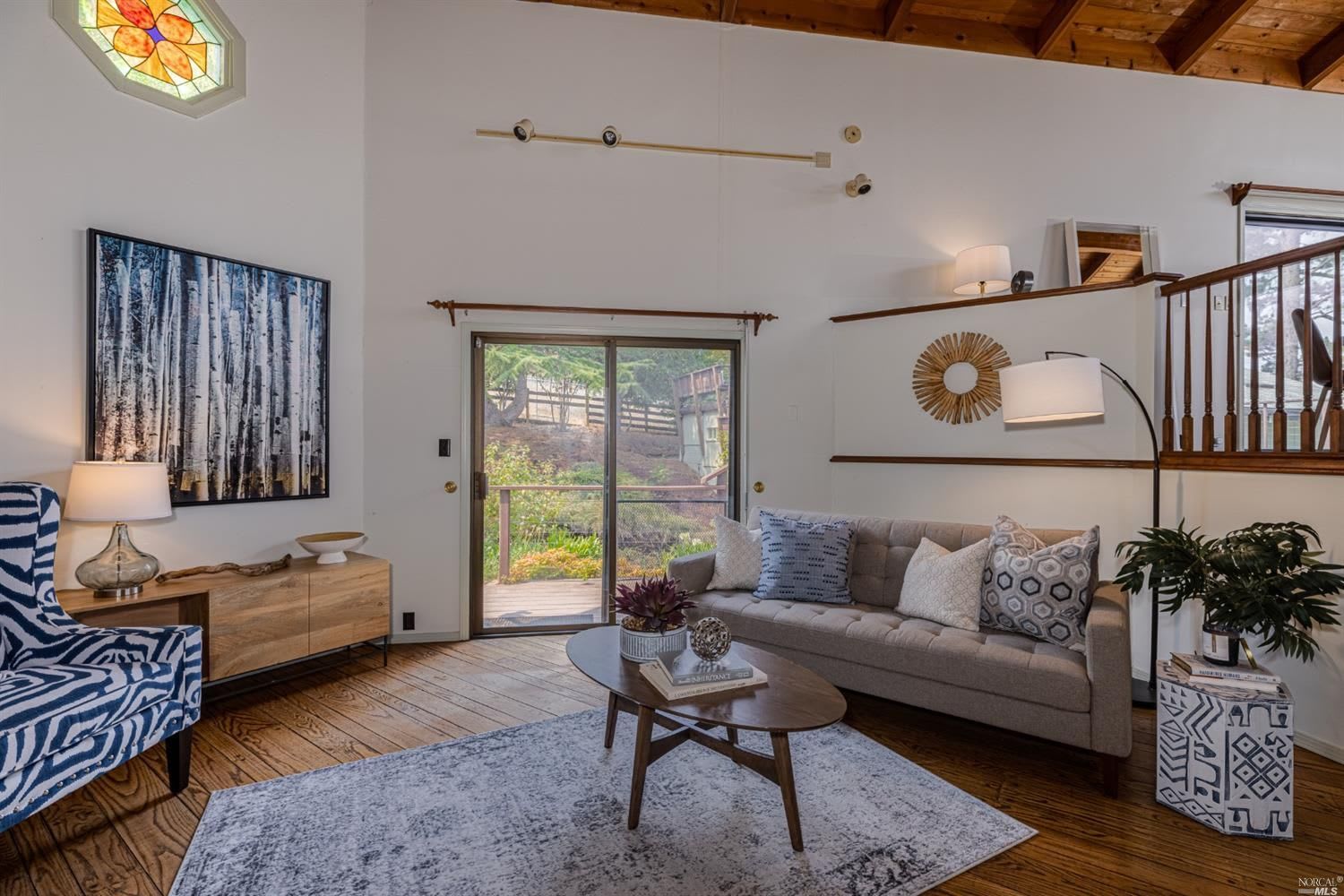 Living room with a gray sofa, patterned blue armchair, exposed timber ceiling, and sliding glass door.