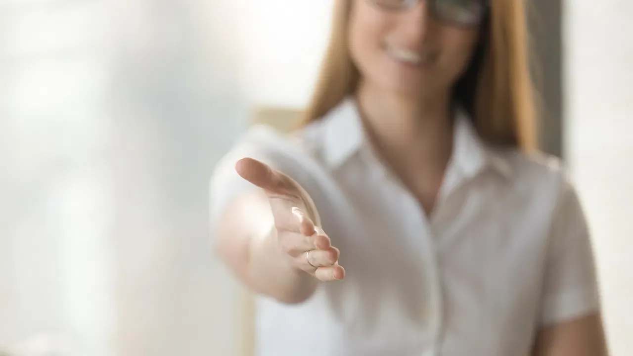 Smiling woman extends her hand for a handshake.