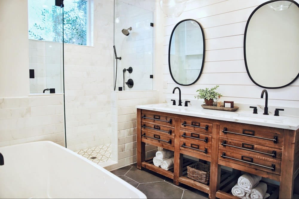 A bathroom with a double vanity, a walk-in shower, two white sings and two large mirrors.