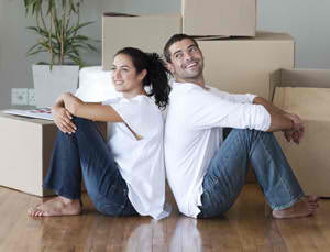 Couple sitting back to back on the floor among moving boxes.