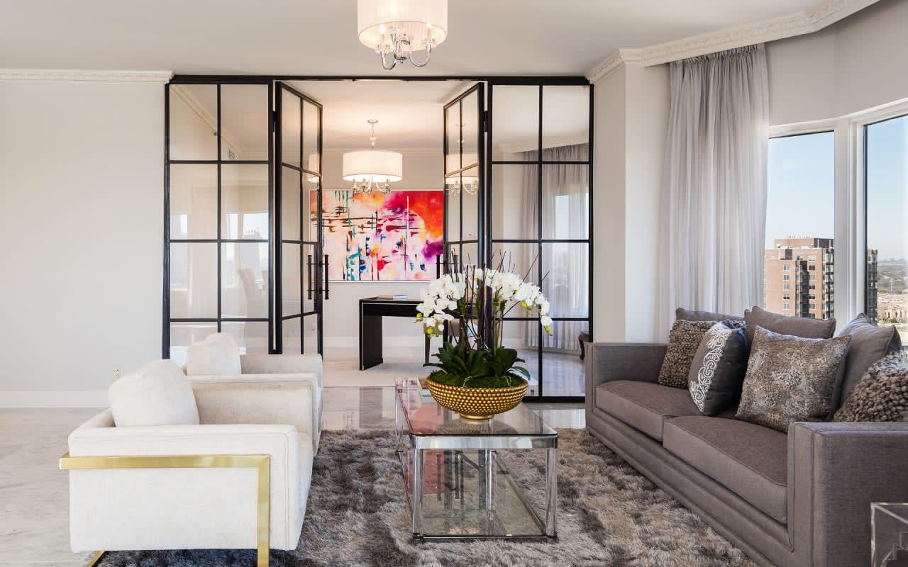 Chic seating area in a high-rise condo, near an office with oversized black-framed glass doors, offering a contemporary feel.