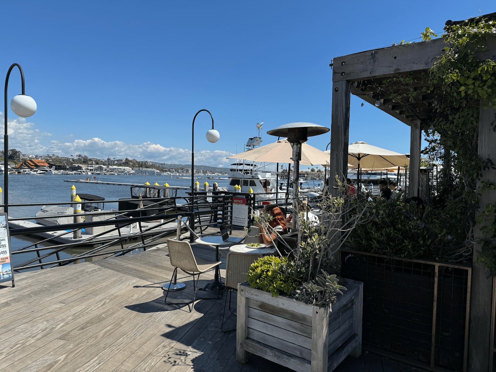 Outdoor patio dining area by the water with views of boats and Newport Beach skyline.