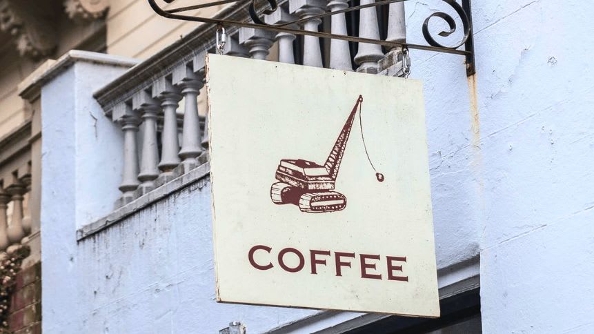 The sign at Coffee Roasters features an artful illustration: a crane, reminiscent of a coffee pot, gracefully pouring out its aromatic brew. Boldly written below, the word “COFFEE” beckons passersby to step inside and savor the magic.