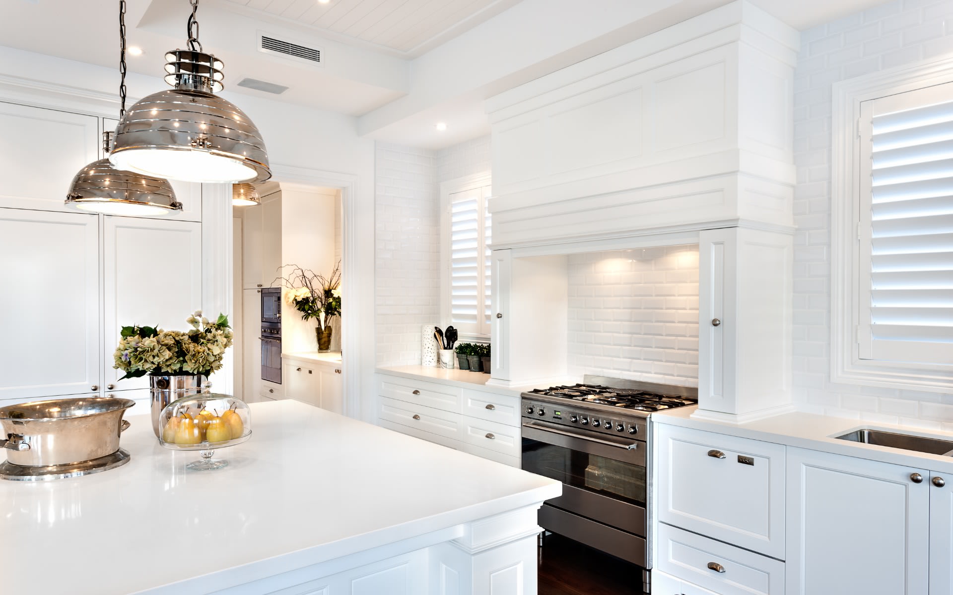 A white kitchen with a stove and a sink. The kitchen has stainless steel appliances and granite countertops.