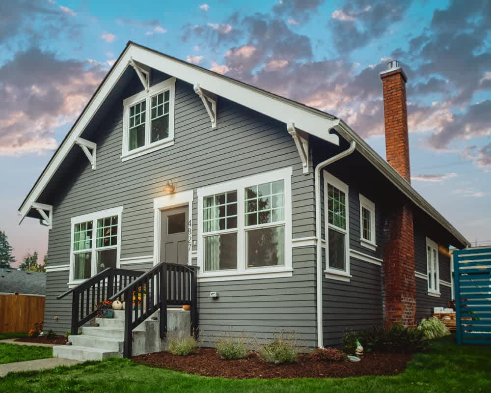 Gray gable-front house with white trim, a brick chimney, and black-railed front steps.