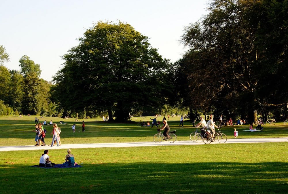 busy park in Columbus, IN with people walking and biking on a path and sitting on blankets in the grass