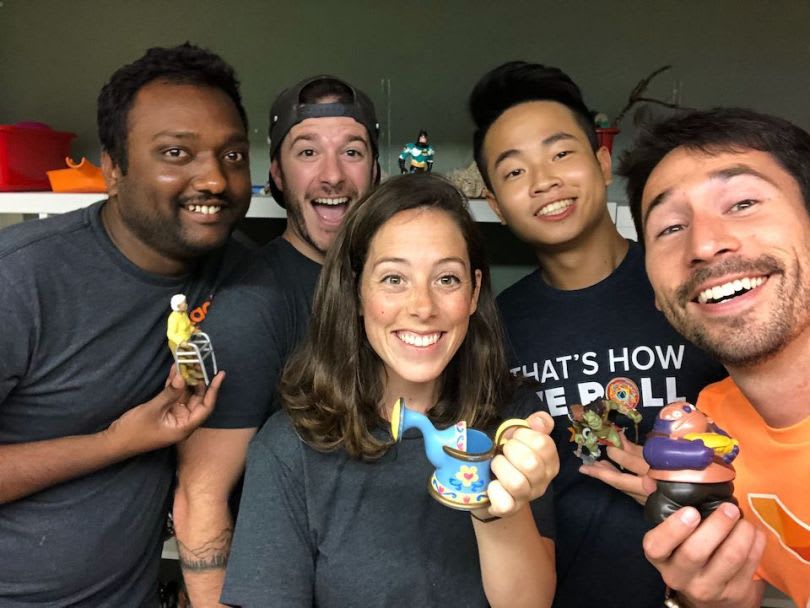 Five adults smile for a group selfie while holding colorful toys.