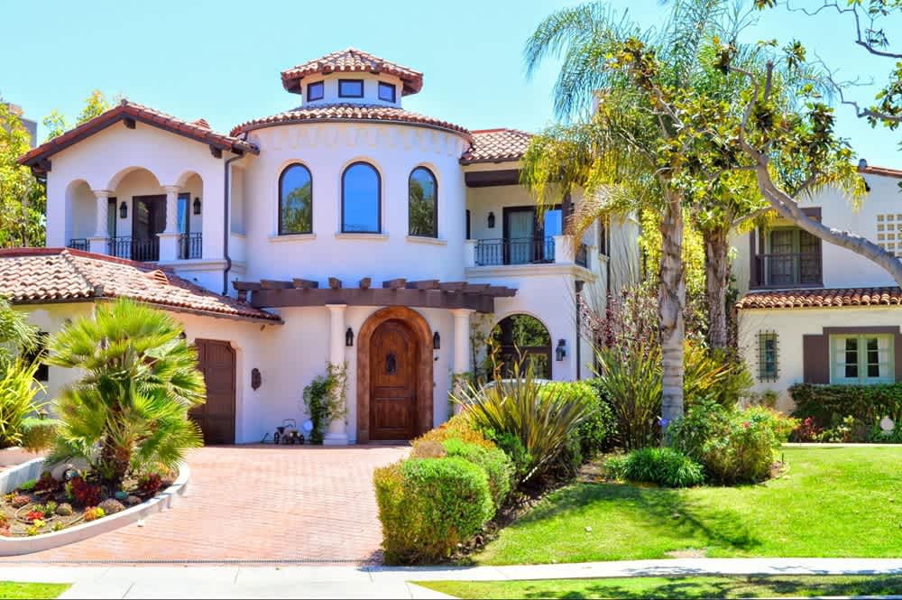 Mediterranean-style home with arched windows, terracotta roof, and lush landscaping.