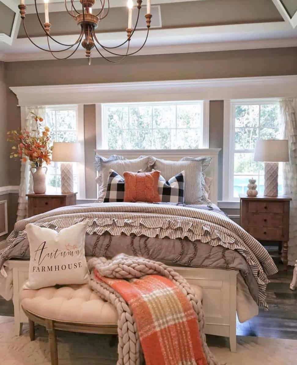 A cozy bedroom featuring a bed with patterned bedding, decorative pillows, a plush throw, and warm lighting from a chandelier.