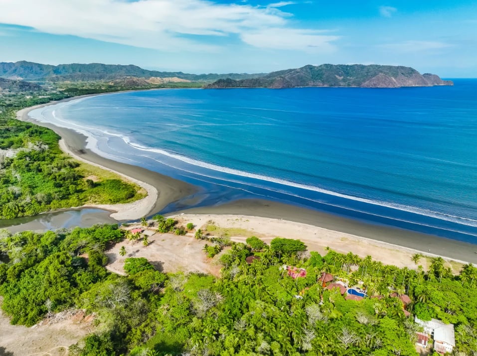 Lush green mountains line the background, with wispy clouds in a clear blue sky. The atmosphere is serene and tropical.