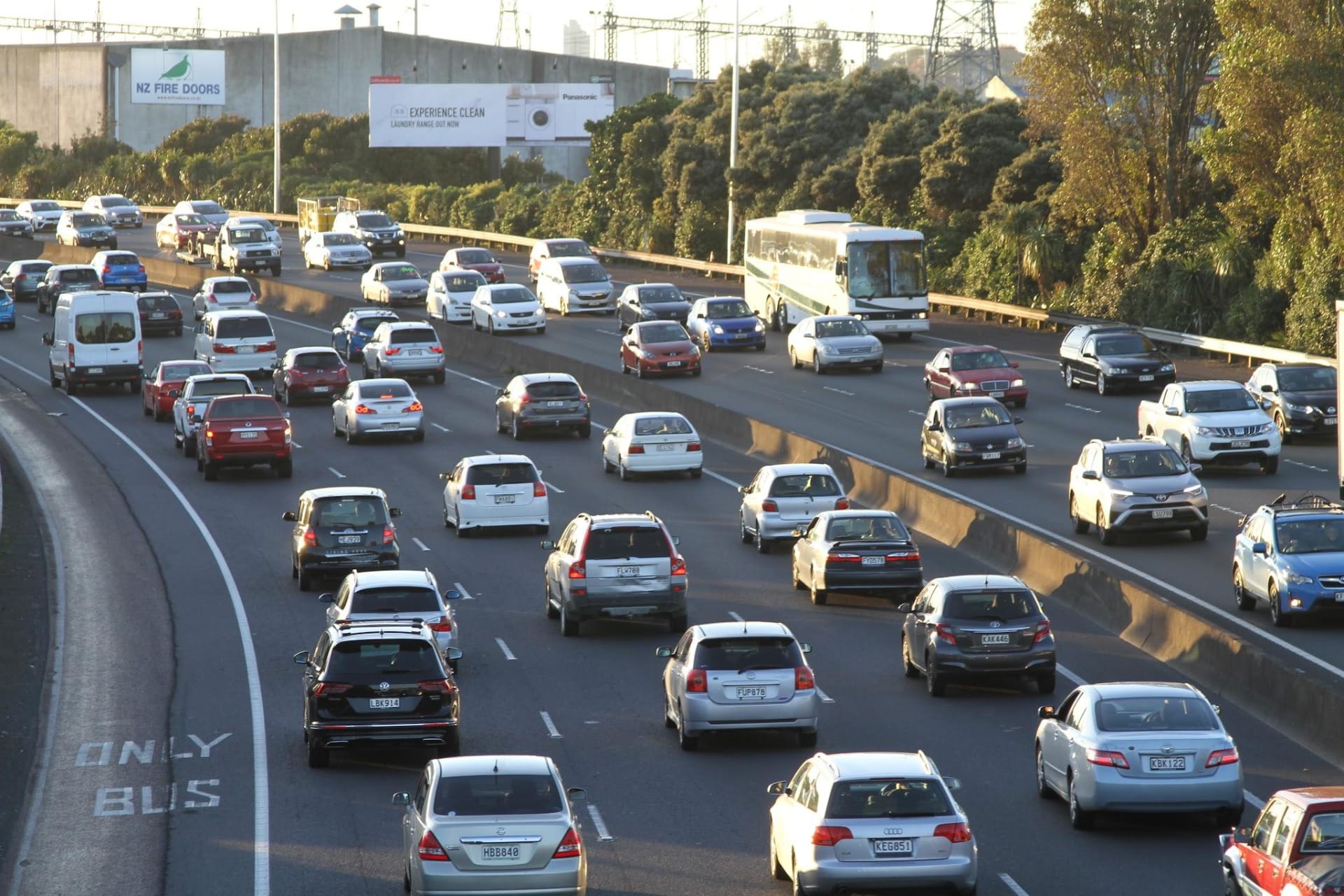 A busy highway scene with various cars and a bus, surrounded by greenery and urban structures.
