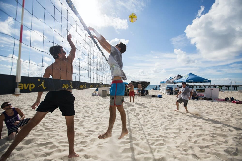 Man in white shirt and blue shorts playing volleyball on beach during daytime