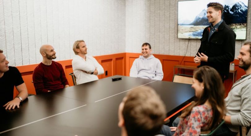 Coworkers meet around a conference table as a man speaks in a modern office.