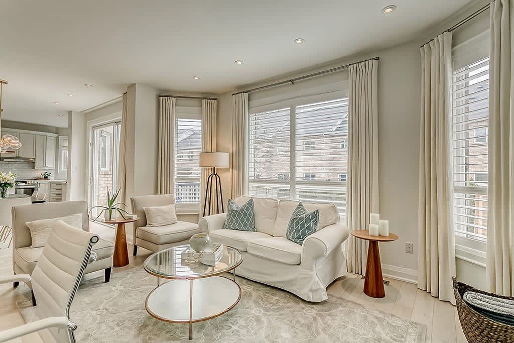 A living room with a white couch, two white chairs with throw pillows, and a metal coffee table with a glass top.