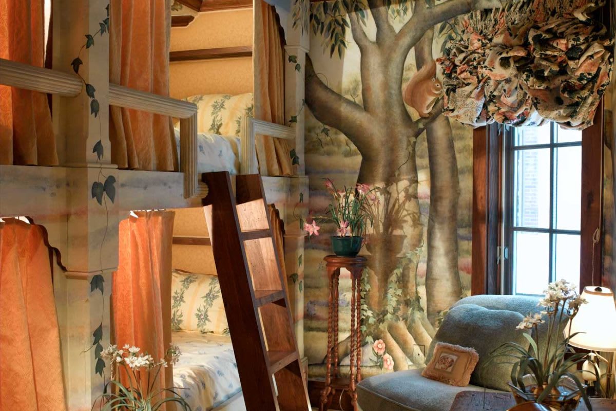 A cozy bedroom with bunk beds and a whimsical mural of a tree and forest scene