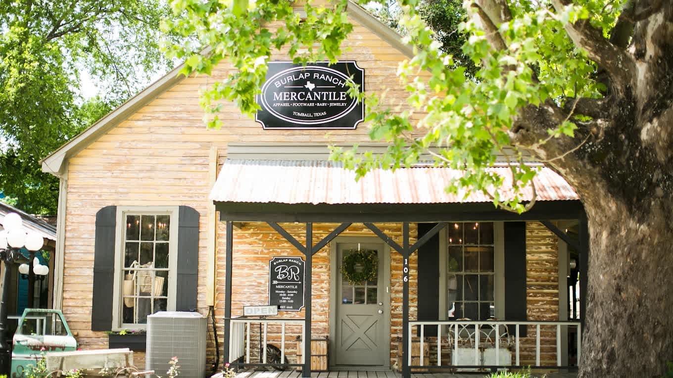 Burlap Ranch Mercantile storefront in Tomball, with a covered porch beneath a large shade tree.