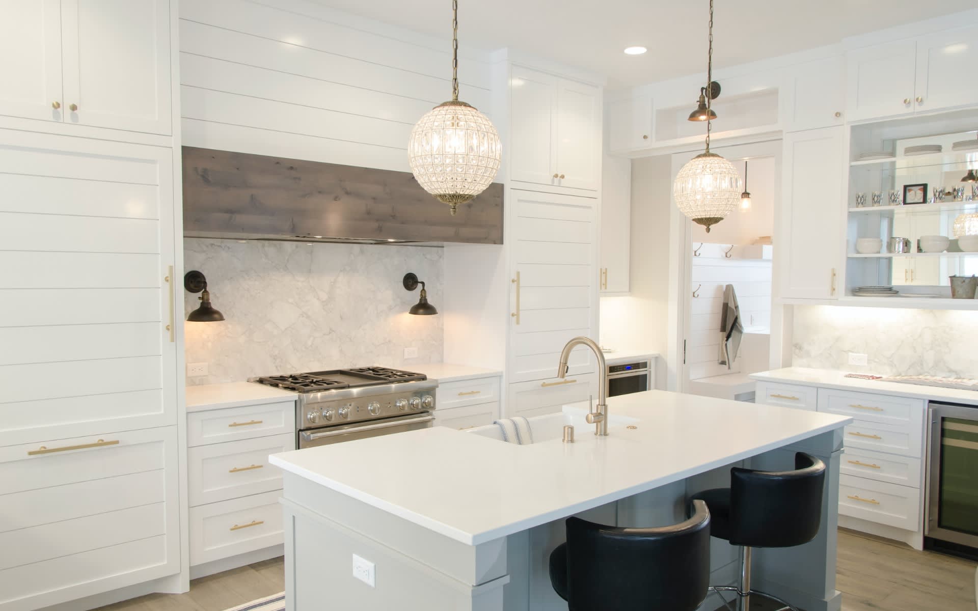 Bright white kitchen with a large island, brass fixtures, marble backsplash, and globe pendant lights.