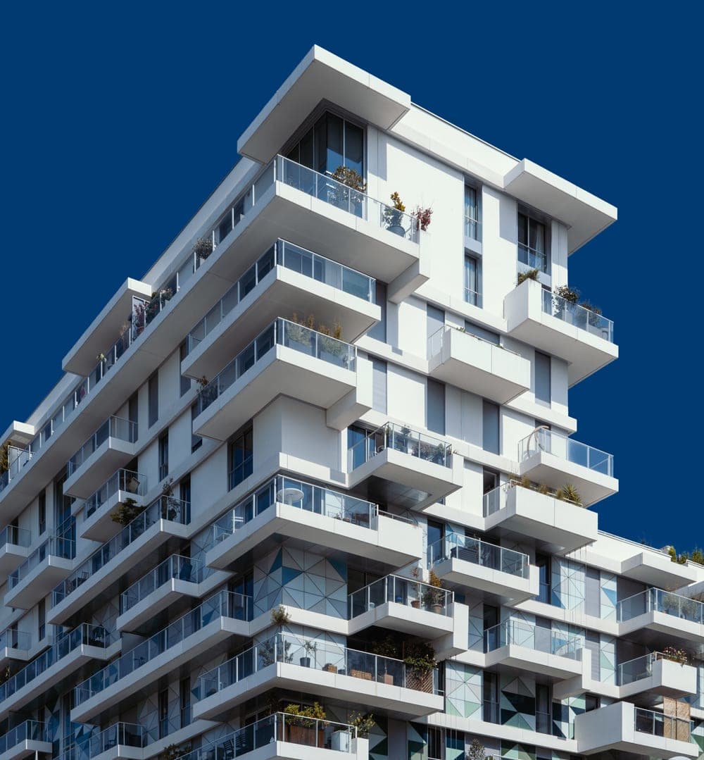 Modern white apartment building with staggered glass-railed balconies against a deep blue sky.